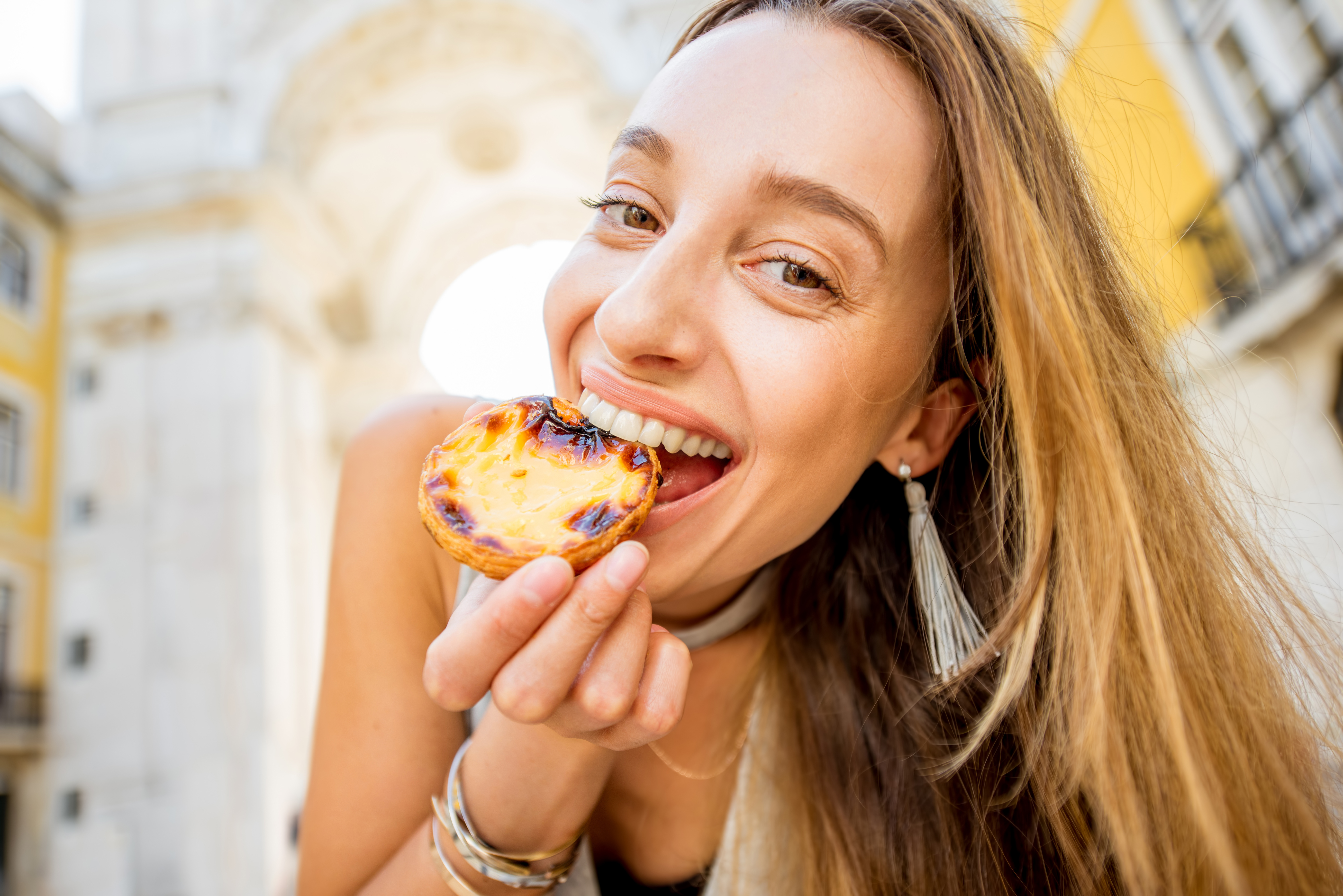 Woman traveling in Lisbon, Portugal Young woman holding portuguese egg tart pastry called pastel de Nata outdoors on the triumphal arch background in Lisbon