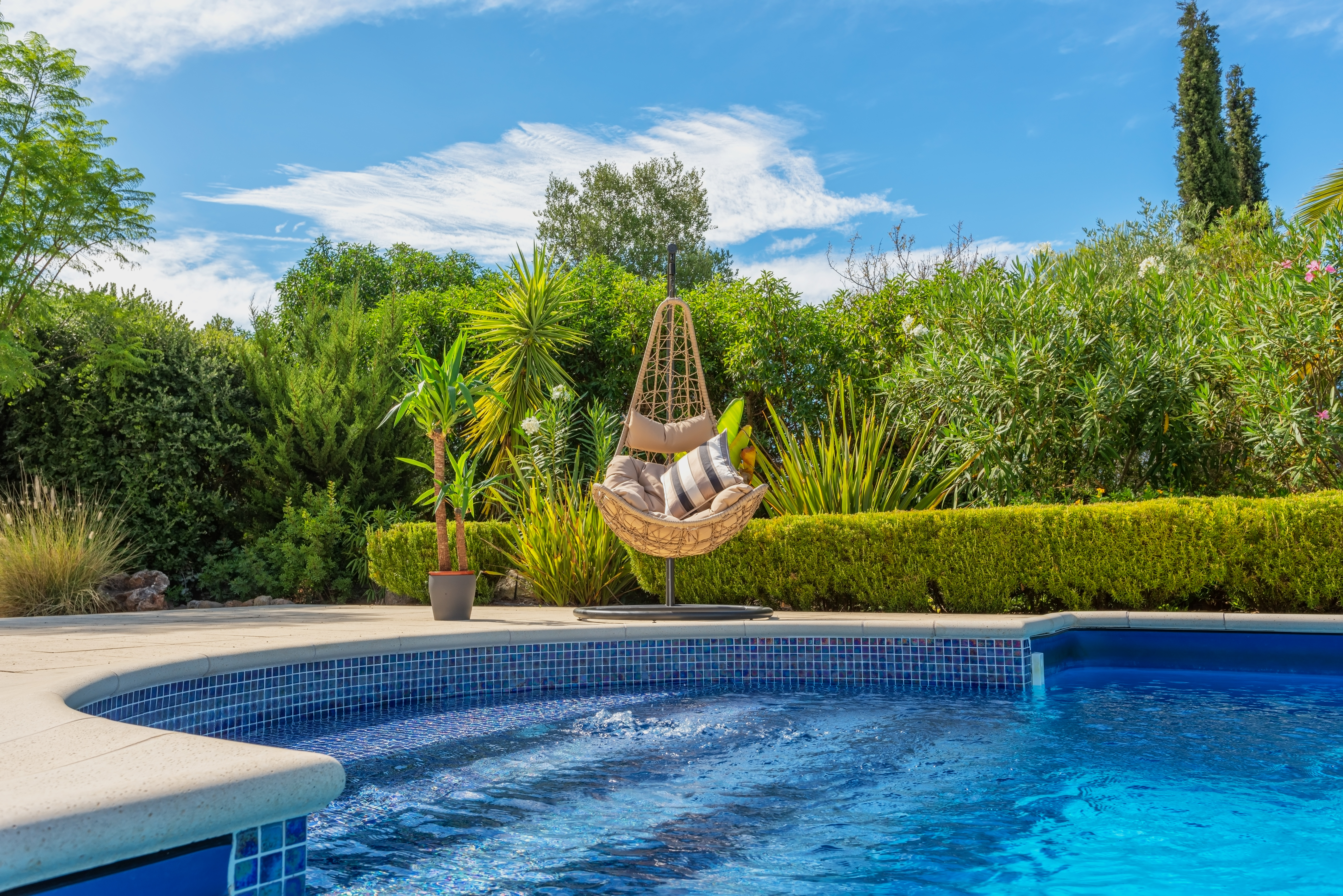 Luxurious pool in the garden of a private villa, hanging chair with pillows for leisure tourists, in summer. Portugal, Algarve. Luxurious pool in the garden of a private villa, hanging chair with pillows for leisure tourists, in summer. Portugal, Algarve